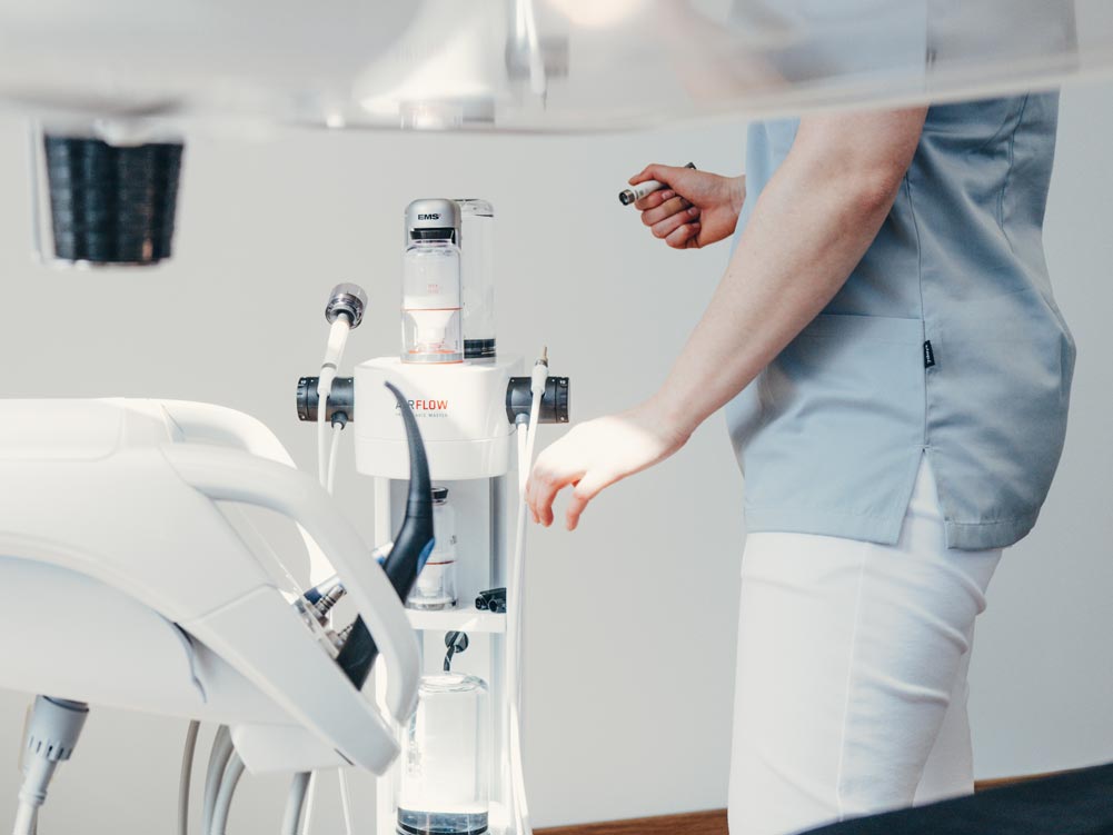 Detailaufnahme eines Air Flow Geräts in der Zahnarztpraxis Petsos&Zahn, welches zur professionellen Zahnreinigung genutzt wird. Es sind die Hände und ein Teil des Körpers einer Mitarbeiterin zusehen, die das Gerät vorbereitet.