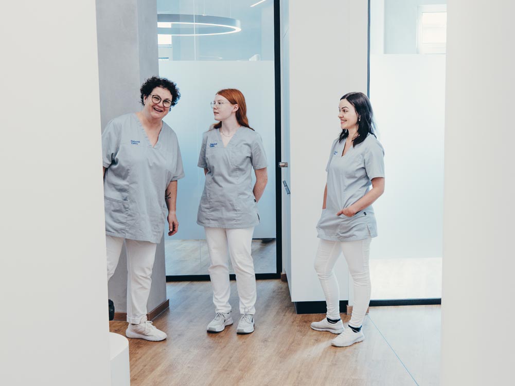 Drei Mitarbeitende der Praxis Petsos&Zahn in Soest stehen gut gelaunt nebeneinander